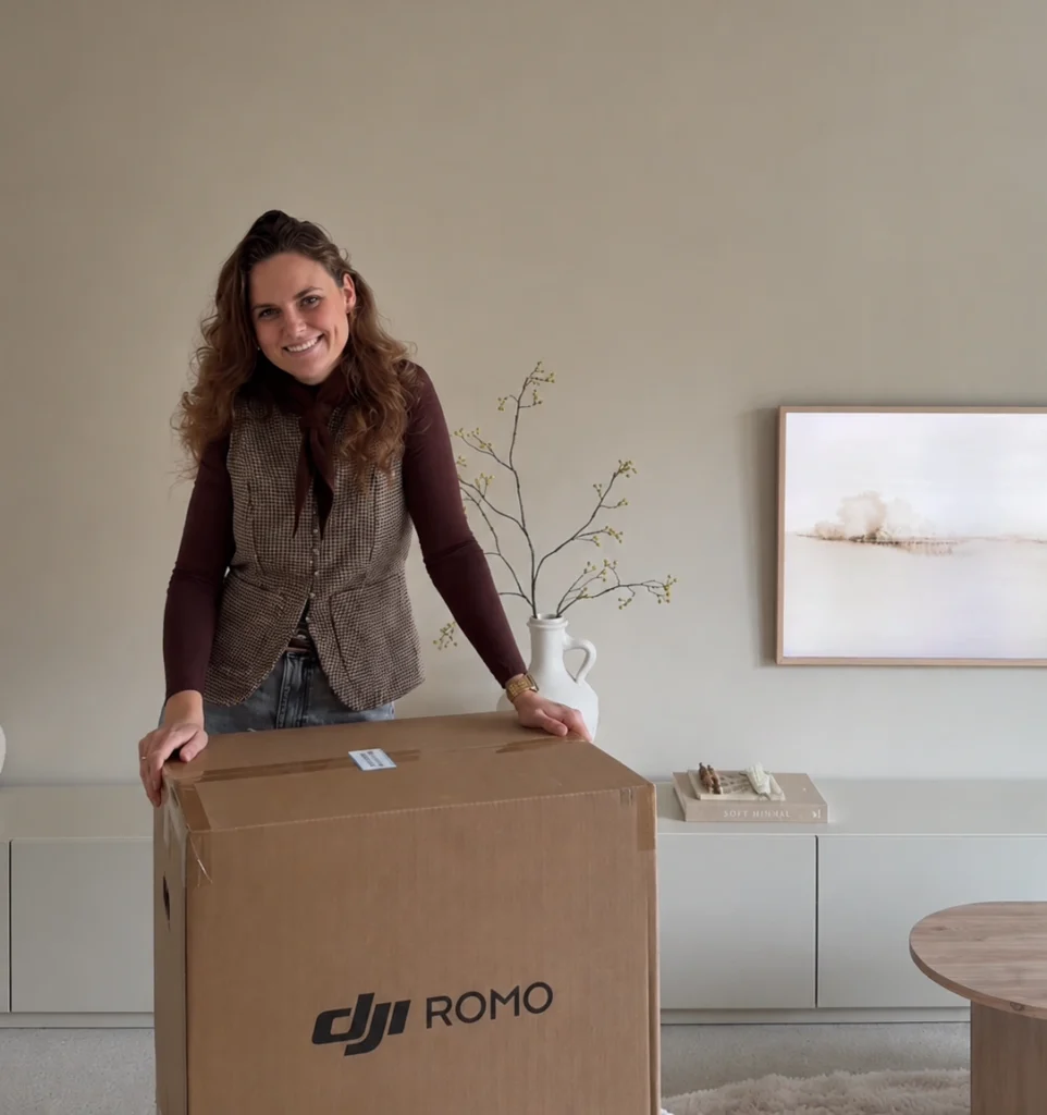 Alena Pruim-de Ruiter staat achter een doos van de DJI ROMO-robotstofzuiger in een lichte woonkamer